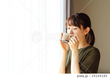 窓際でコーヒーを飲む女性の写真素材
