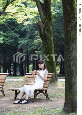 公園のベンチで本を読む女性 24190613
