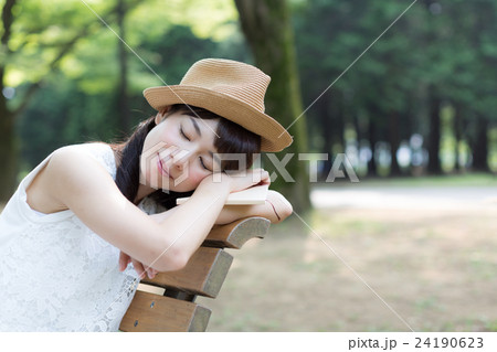 公園のベンチでくつろぎながら本を読む女性 24190623