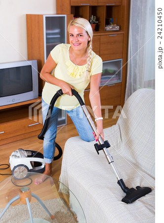 Blonde girl hoovering in living room . 24210450