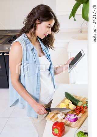 Young woman using digital tablet while chopping vegetables 24217779
