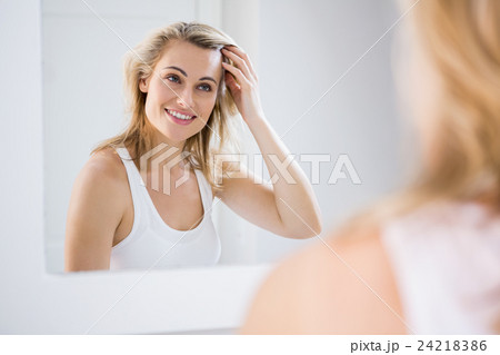 Young woman checking her hair in bathroom mirror 24218386