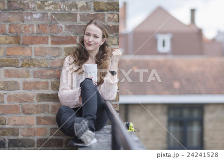 Mid-adult woman sitting on balcony railing and leaning against brick wall 24241528