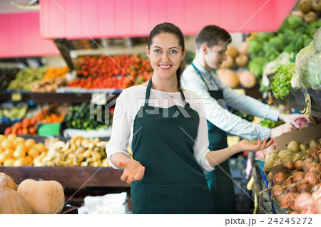 Friendly positive sellers having vegetables and fruits on displays Friendly positive sellers having vegetables and fruits on displays 24245272