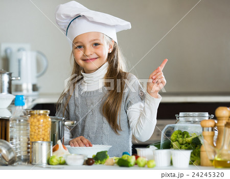 Smiling female child in chef cap with vegetables in kitchen 24245320