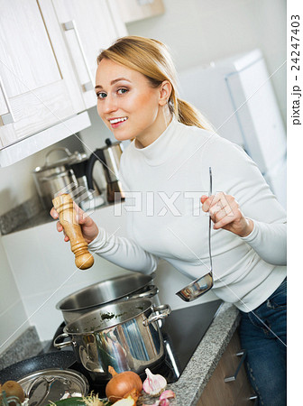 Smiling long-haired girl cooking soup at kitchen stove 24247403