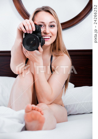 Laughing woman lying in the bed and holding a camera 24266252