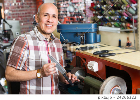 Workman resharpening knives on machine. 24266322