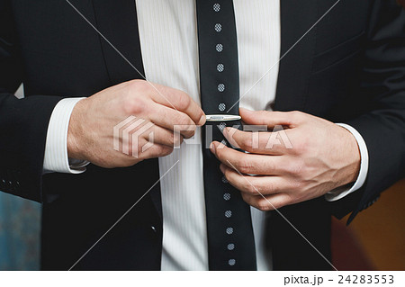 Man in black suit putting on tie clip Man in black suit putting on tie clip 24283553