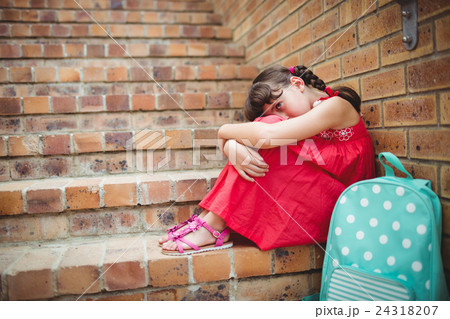 Sad brunette girl seated against a brick wall 24318207