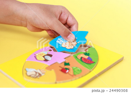 Hand of kid holding wooden jigsaw of the 5 food Groups. Child development concept Hand of kid holding wooden jigsaw of the 5 food Groups. Child development concept 24490308