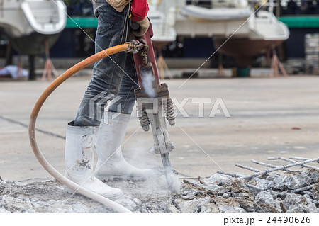 Construction worker removes excess concrete with drilling machine 24490626