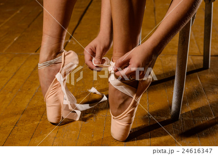 Ballerina tying pointe ballet shoes on stage 24616347