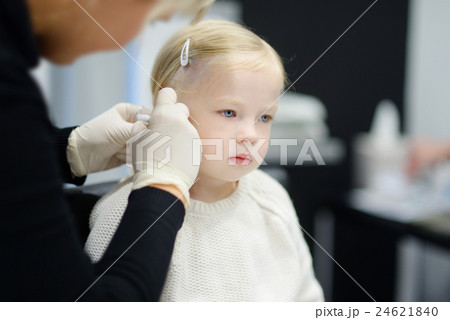 Adorable little girl having ear piercing process in beauty center 24621840