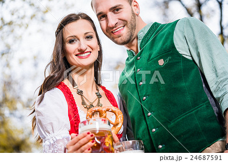 Couple in Dirndl and Tracht having Pretzel  24687591