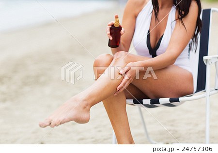 woman spraying sunscreen oil to her skin on beach woman spraying sunscreen oil to her skin on beach 24757306