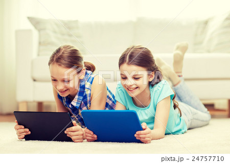 happy girls with tablet pc lying on floor at home 24757710