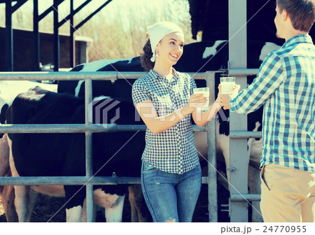 Cheerful boy and girl farmers standing with in the cow hangar and showing fresh milk Cheerful boy and girl farmers standing with in the cow hangar and showing fresh milk 24770955