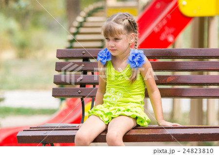 Portrait of upset five year old girl who is sitting on the bench on the background of the playground Portrait of upset five year old girl who is sitting on the bench on the background of the playground 24823810