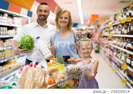 Happy family standing with full cart in supermarket Happy family standing with full cart in supermarket 24826914
