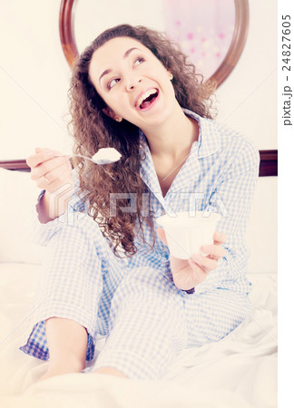 Curly haired woman with tasty yoghurt in bed 24827605