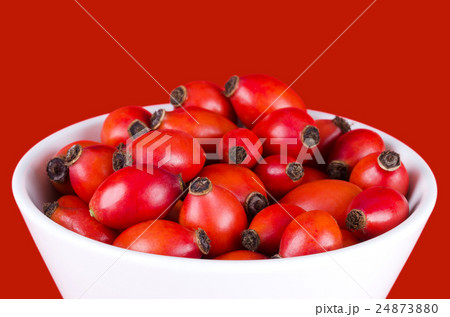 Rose hips in a white bowl over red 24873880