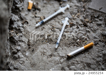 close up of syringe and smoked cigarette on ground close up of syringe and smoked cigarette on ground 24955254