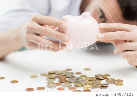 close up of man pouring coins from piggy bank 24957125