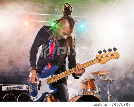 Rock band performs on stage. Bassist in the foreground. 24976302