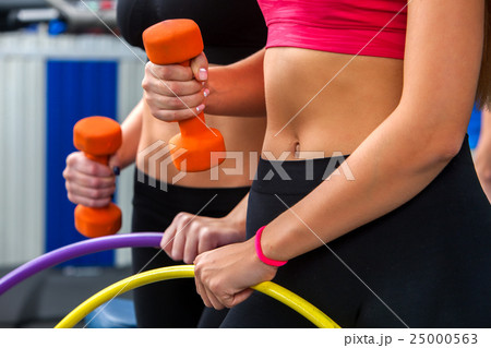 Women with bare belly working dumbbells and hoop 25000563
