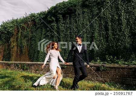 Bride and groom run along the park  25091767