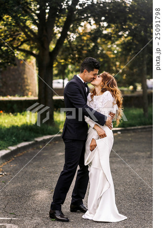 Bride holds her dress while groom hugs her tightly 25091798