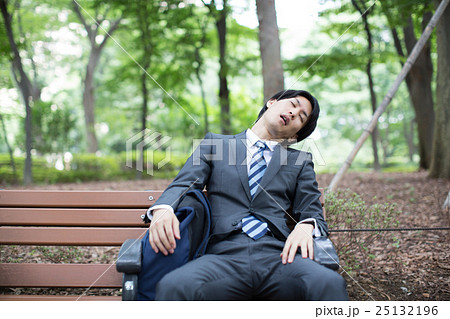 公園のベンチで居眠りするサラリーマンの写真素材