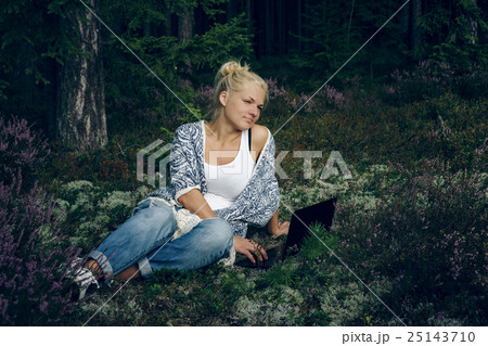 Beautiful young woman sitting on the grass in the 25143710