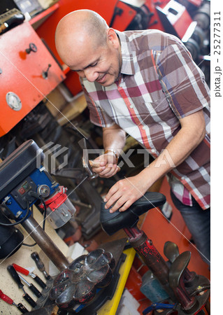 Professional shoemaker heeling footwear on machine 25277311