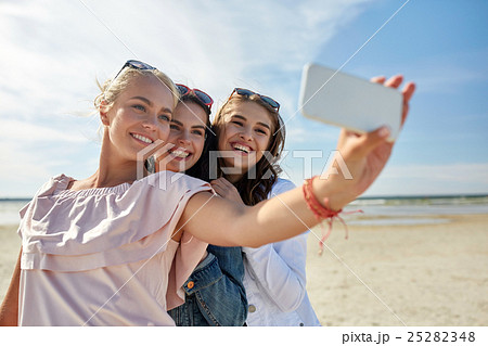 group of smiling women taking selfie on beach 25282348