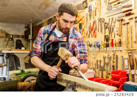 carpenter with wood, hammer and chisel at workshop 25283429