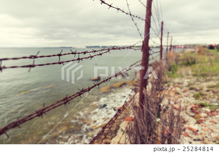 barb wire fence over gray sky and sea barb wire fence over gray sky and sea 25284814