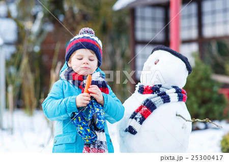 Funny kid boy making a snowman in winter outdoors 25300417