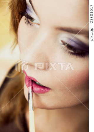 Woman applying pink lipstick with brush 25301017