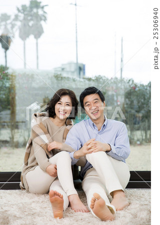 Middleaged Asian Couple Smiling and Sitting on Rug In Livingroom Middleaged Asian Couple Smiling and Sitting on Rug In Livingroom 25306940