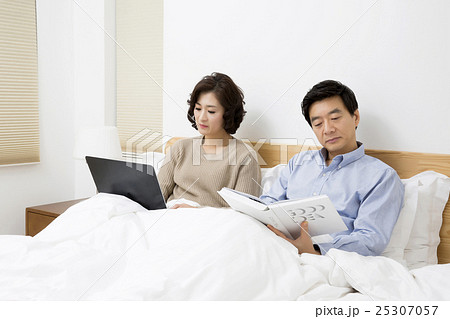 Middleaged Asain Couple in Bed, Wife Looking at a Laptop and Husband Reading Newspaper 25307057