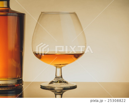 snifter of brandy in elegant typical cognac glass near bottle on table, warm style snifter of brandy in elegant typical cognac glass near bottle on table, warm style 25308822