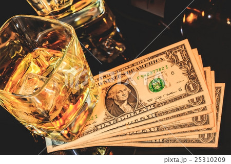 Top of view of glasses of whiskey near bottle on dollars money on a black table. Western theme style 25310209