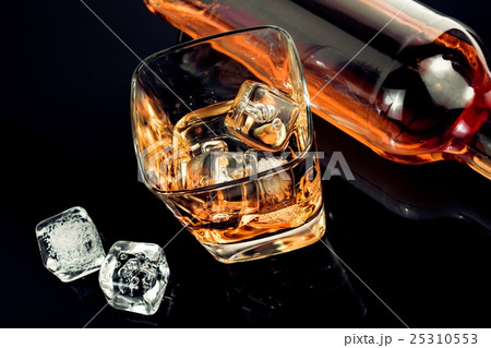 top of view of glass of whiskey near bottle and ice cubes on black table with reflection 25310553