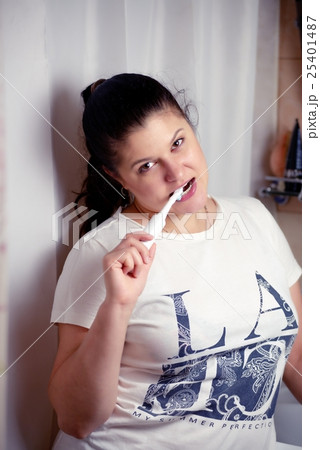 Young woman brushes teeth in bathroom an electric brush Young woman brushes teeth in bathroom an electric brush 25401487