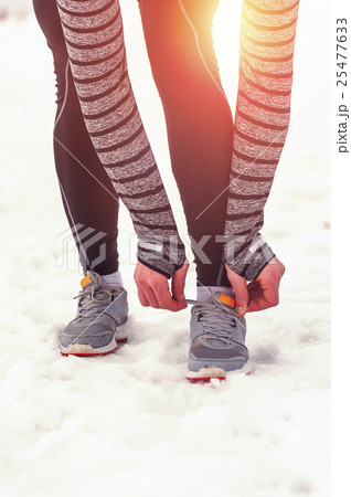Young runner tying shoelaces outdoors in winter Young runner tying shoelaces outdoors in winter 25477633