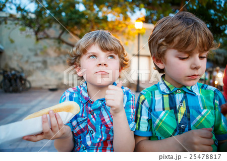 Two little kid boys eating hot dogs outdoors Two little kid boys eating hot dogs outdoors 25478817