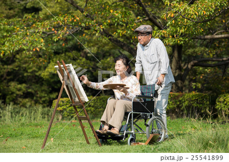趣味の絵画を楽しむ車いすに乗った初老の妻と介助する夫 25541899