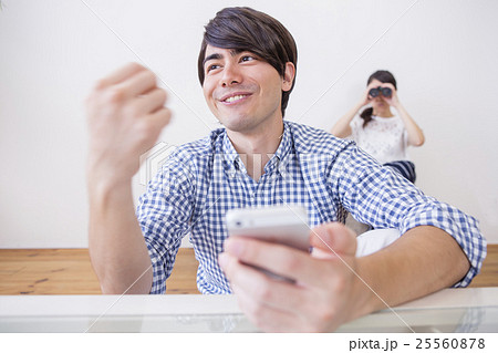 スマホをいじる男性と後ろから見る女性 スマホをいじる男性と後ろから見る女性 25560878
